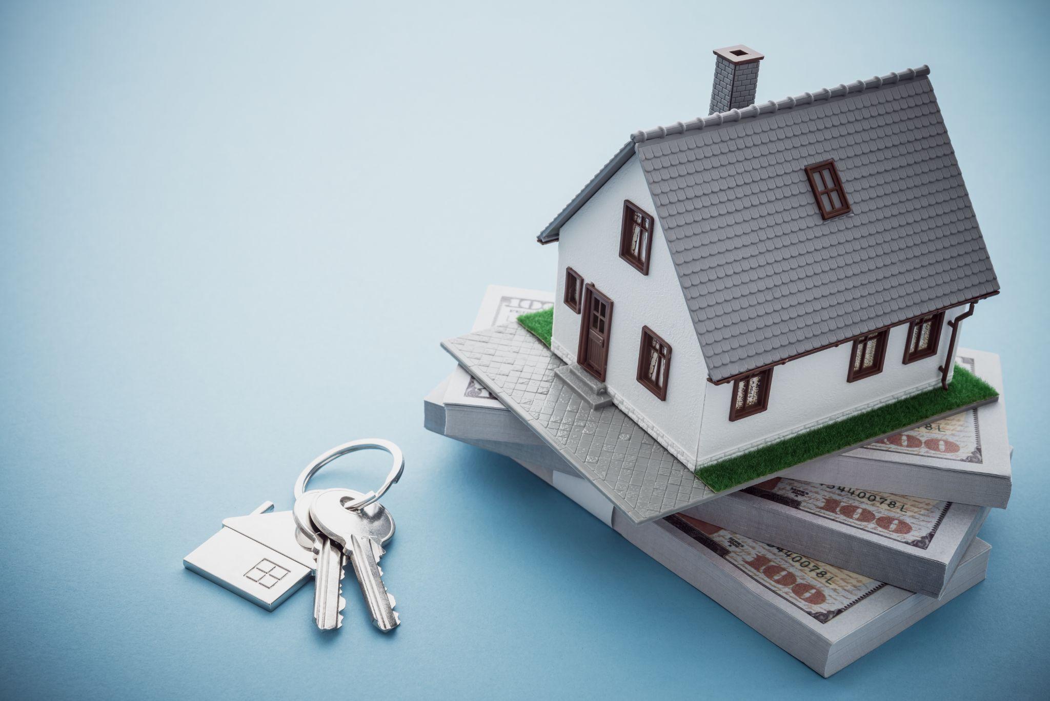 House model, bill dollar banknotes and key on blue background