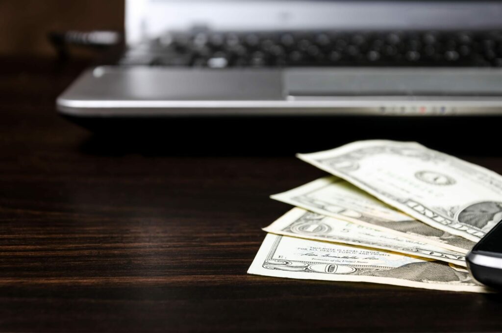 american dollars and laptop computer on a wooden table