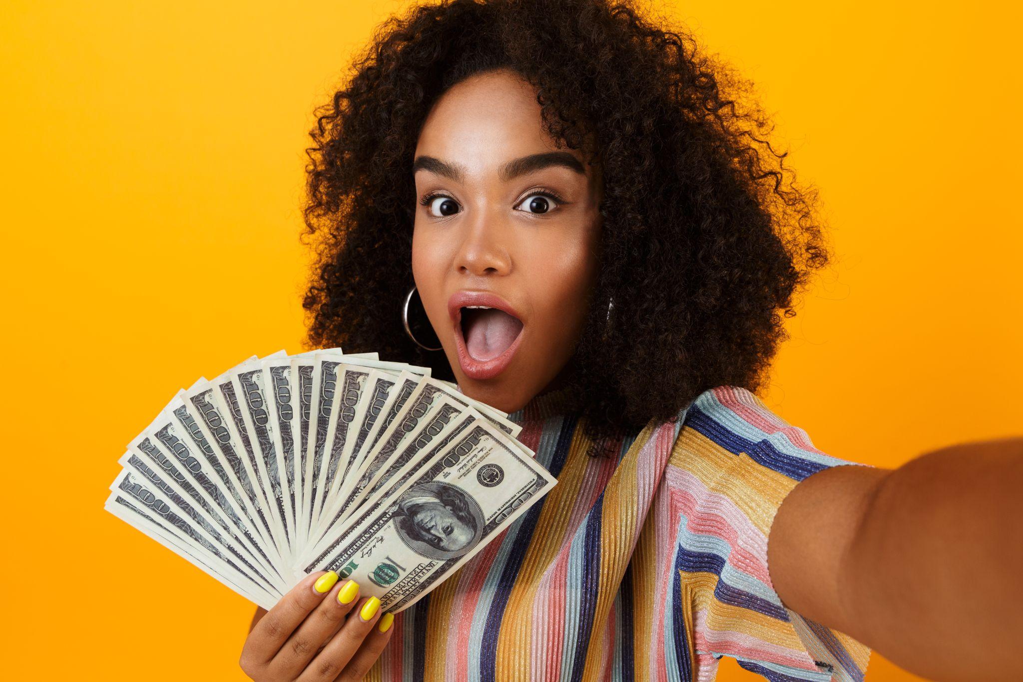 Excited young african woman posing isolated over yellow background holding money make selfie by camera.