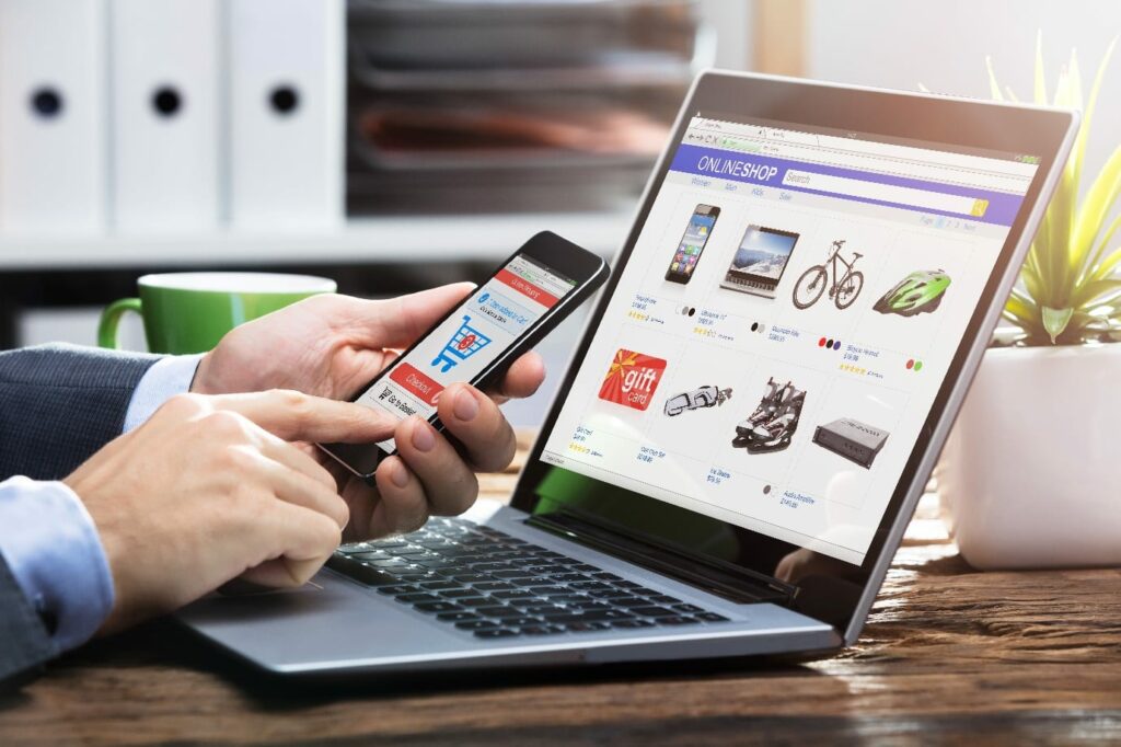 man on smartphone in front of laptop ecommerce shopping online