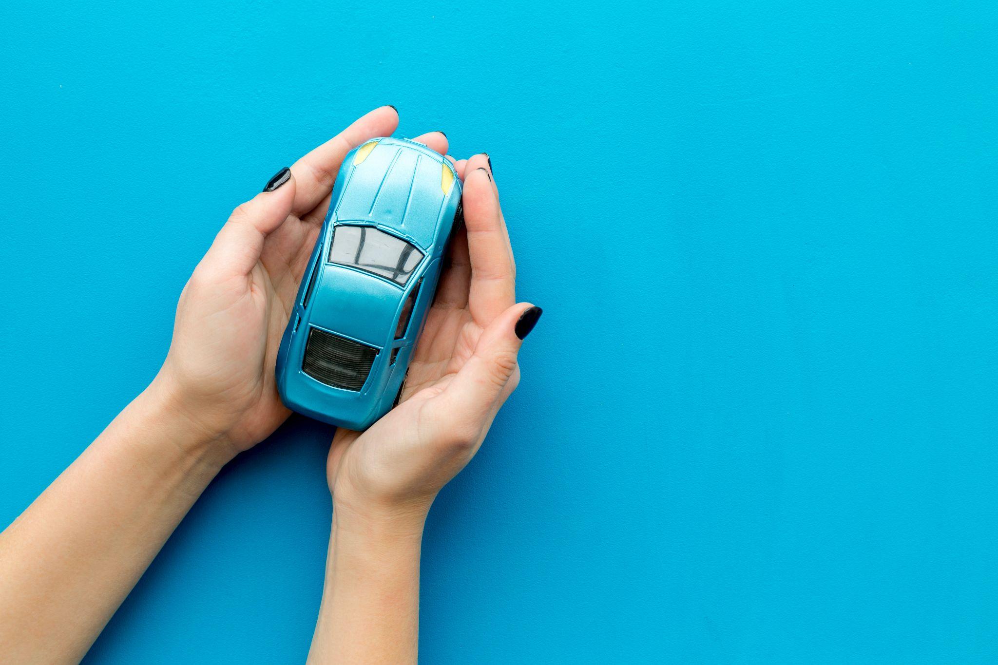 Car toy in female hands on blue background