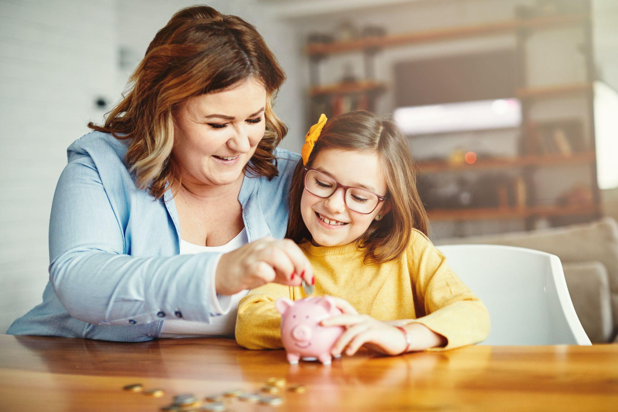 Woman teaching her daughter how to save money in a piggy bank