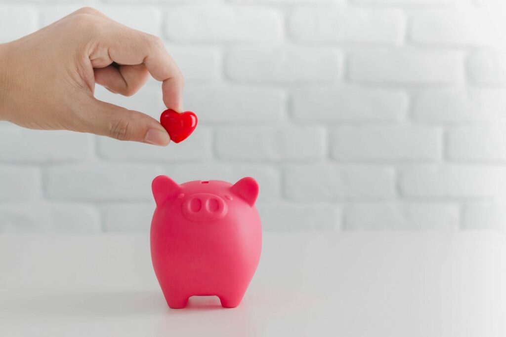 Man's hand putting red heart in to piggy bank