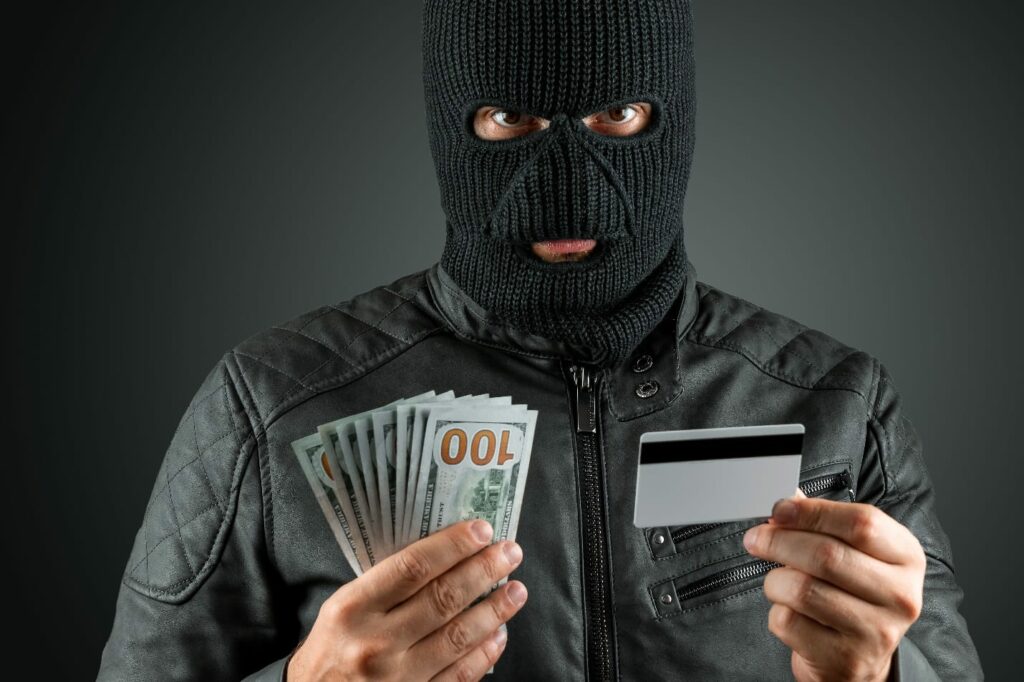 Robber in a balaclava holds a credit card in his hands