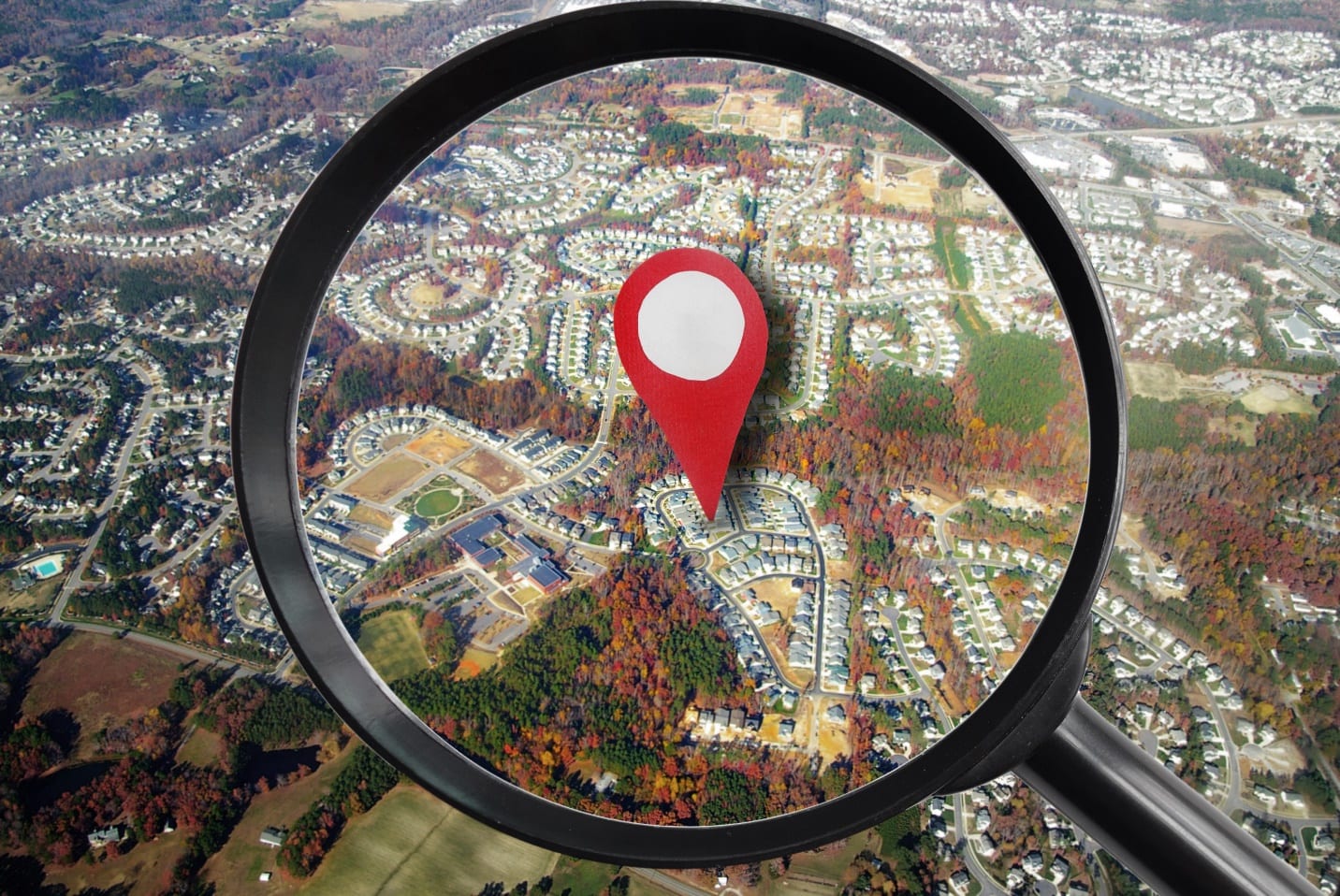 magnifying glass and red locator symbol on house from the air