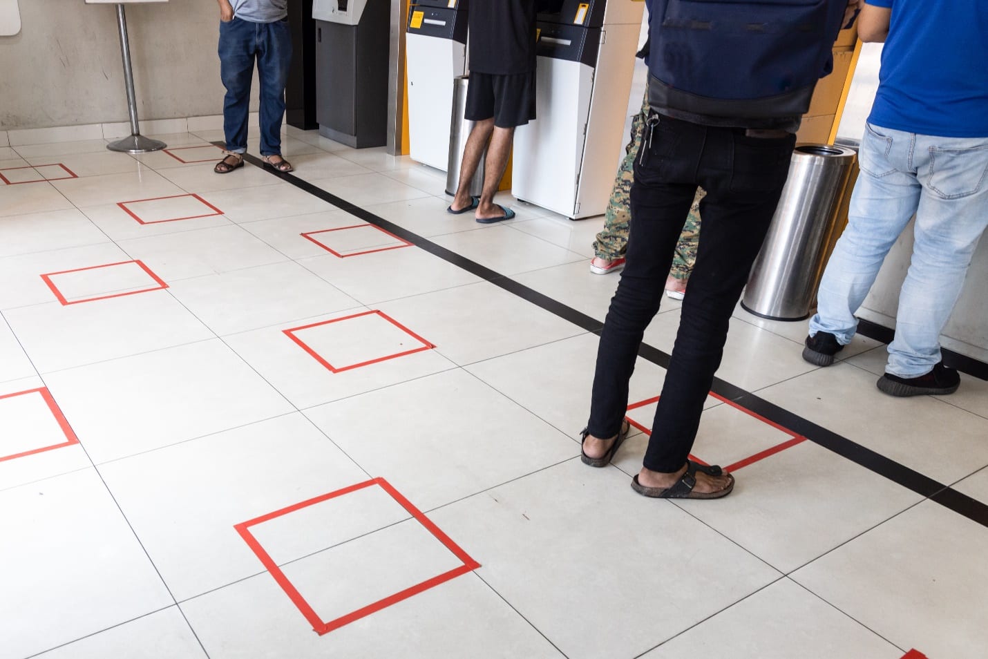 People practicing social distancing in queue towards auto teller machine in bank