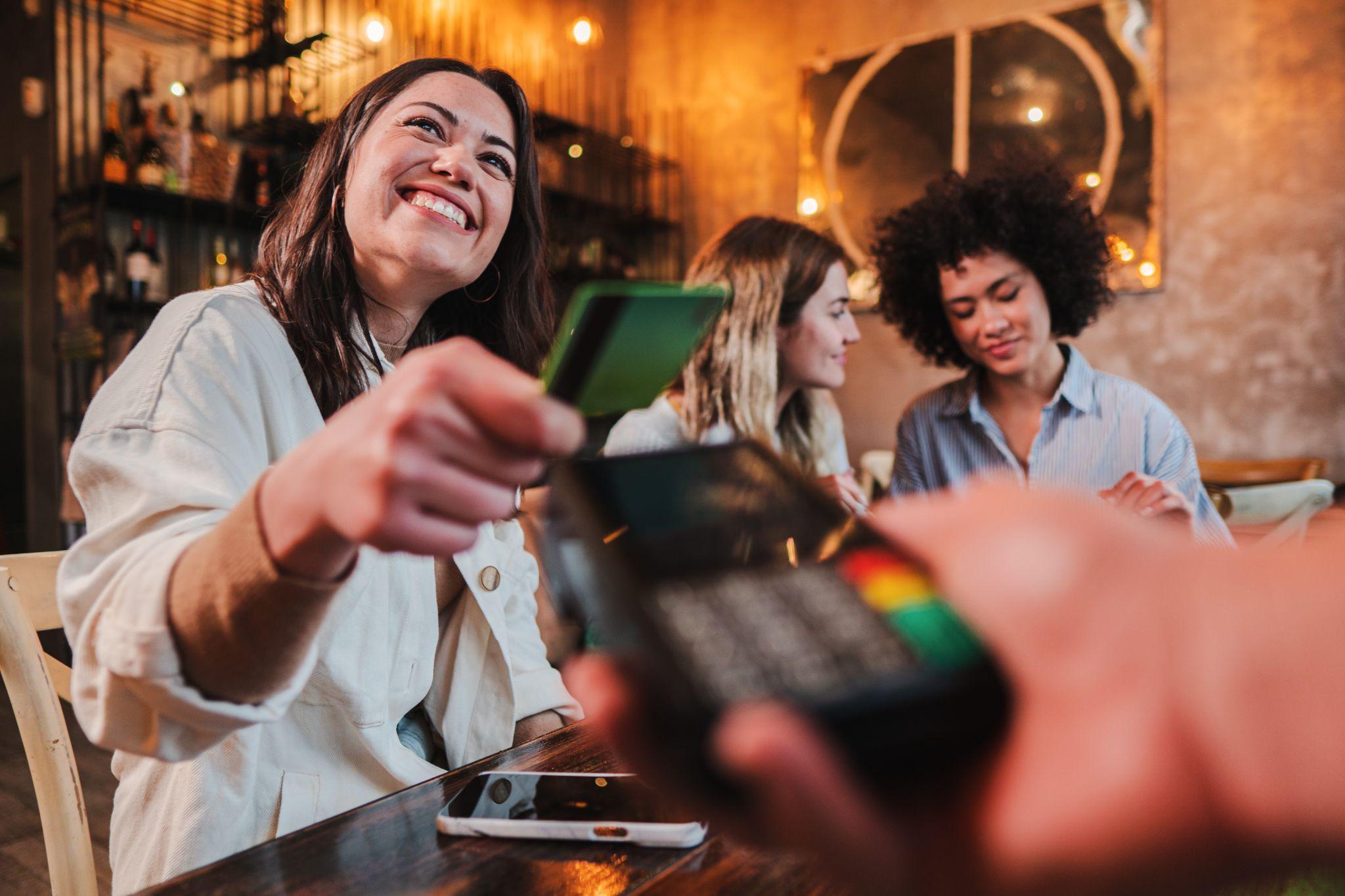 Happy young woman paying bill with a contactless credit card in a restaurant