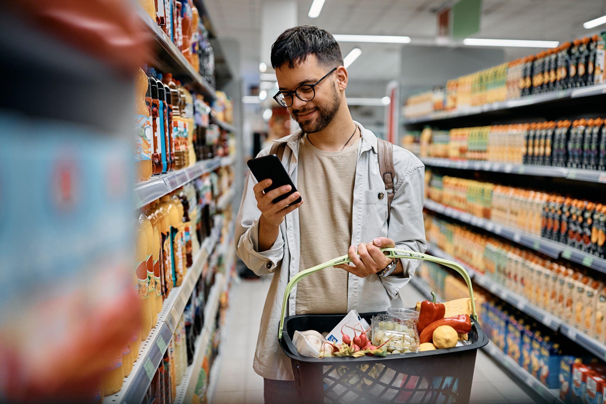 Young man using cell phone while shopping in supermarket