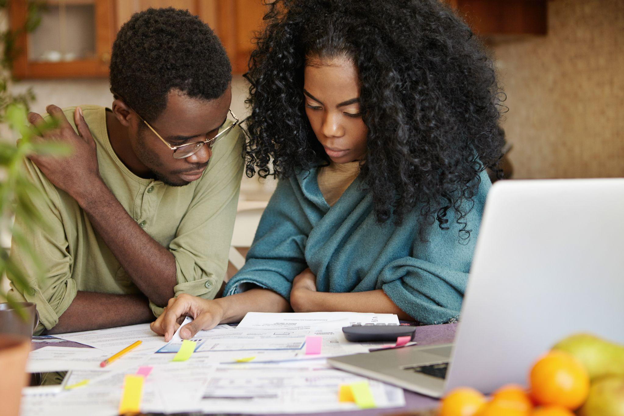 African couple reviewing their finances, analyzing family budget, thinking how to cut off expenses to be able to save money