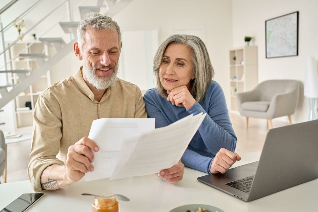 Middle aged senior couple reading paper bills paying bank loan online