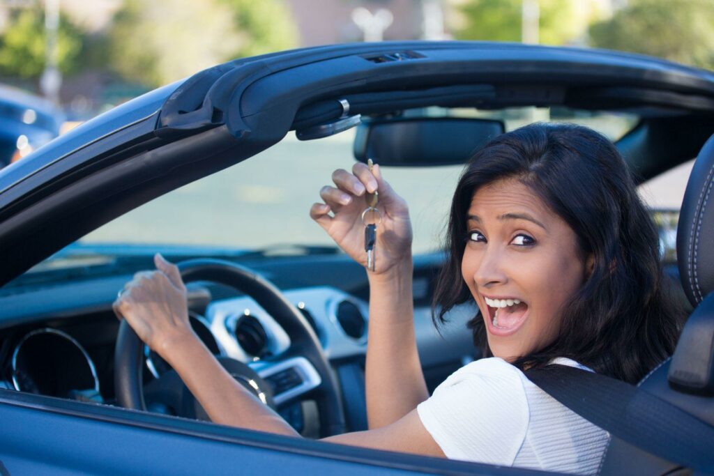 smiling woman holding up keys to her first new car.
