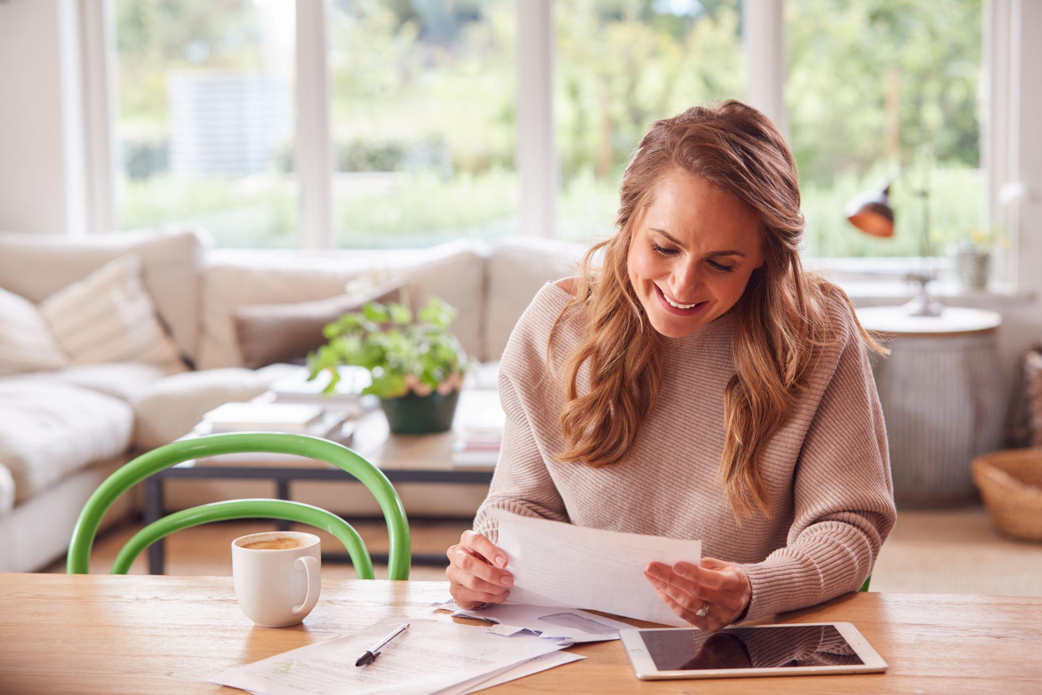 Woman with digital tablet sitting at table at home reviewing domestic finances