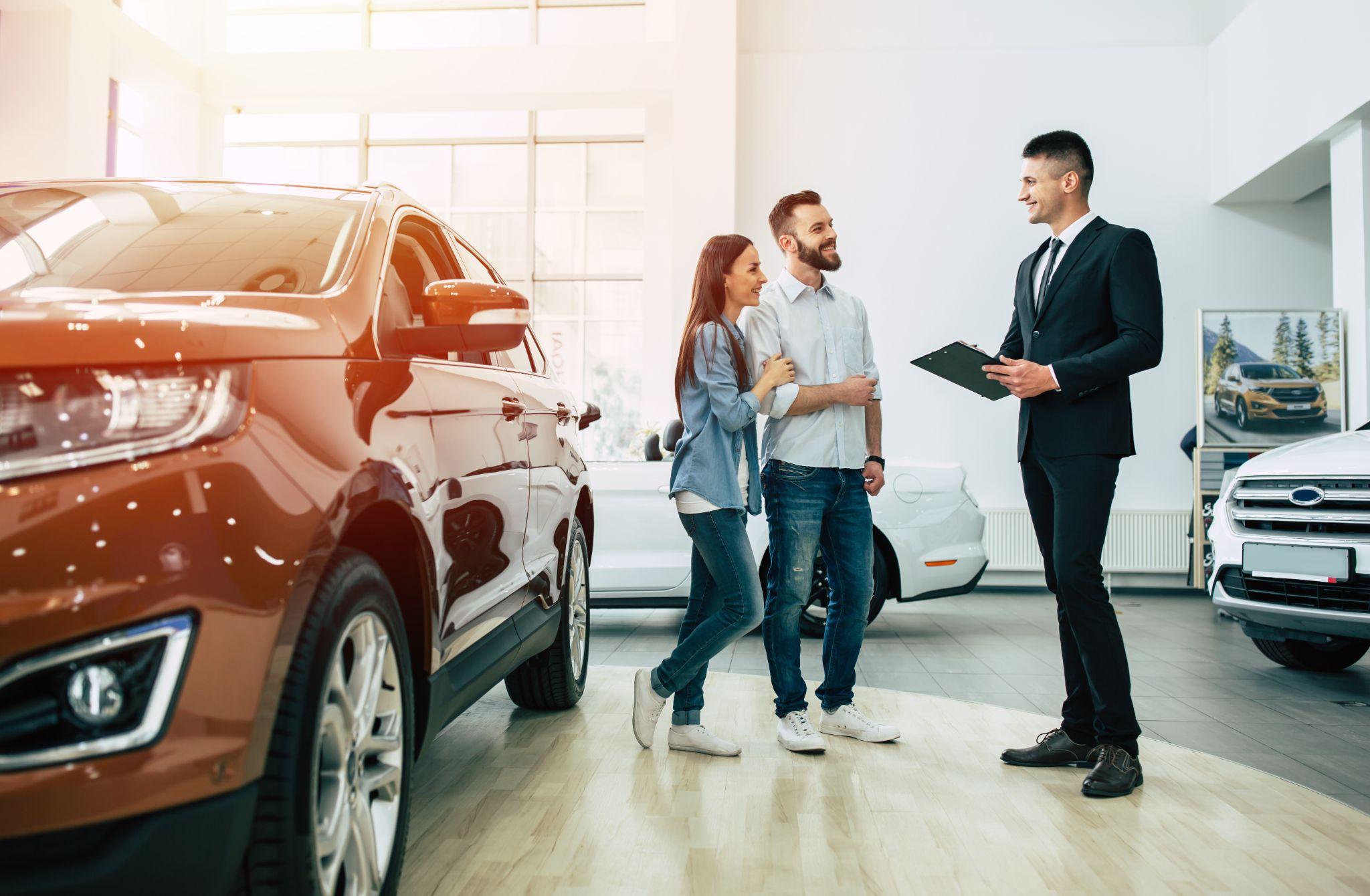 Young modern happy couple buying a new car in city dealership and talking with salesman