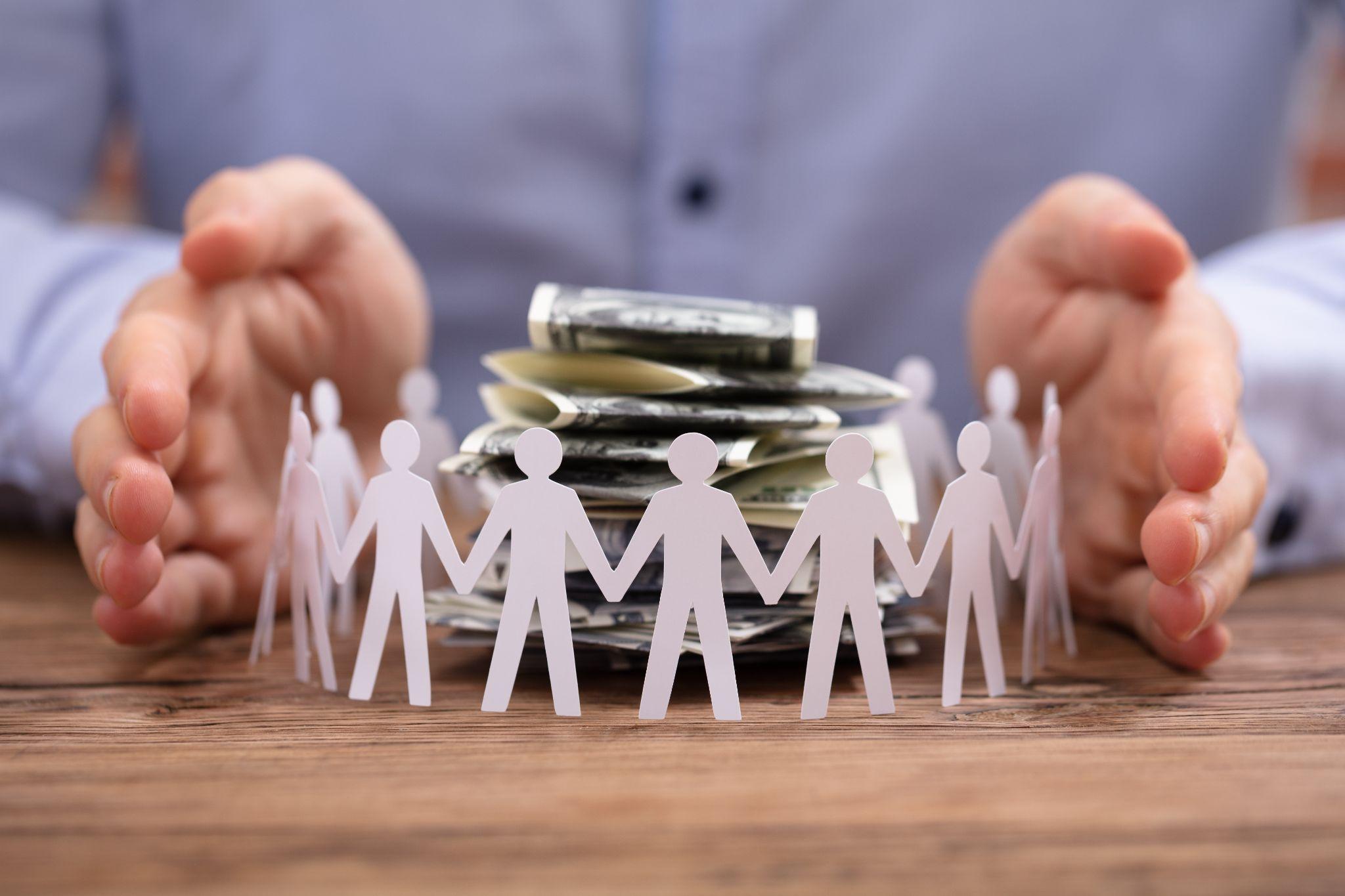 Representation of a not-for-profit financial credit union. Paper cutout of people holding hands surrounding cash money.