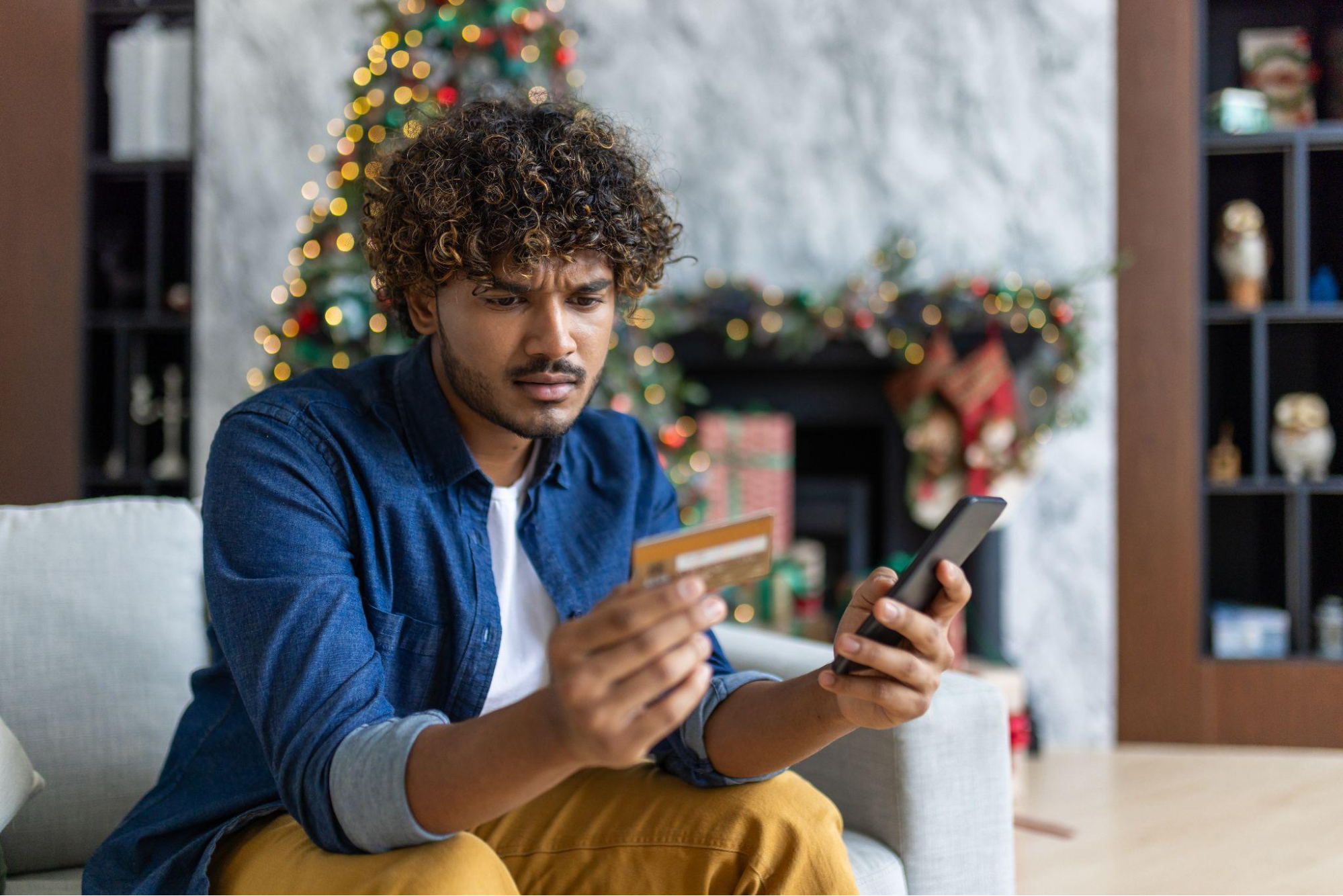 A man looking at his phone and credit card with a confused expression