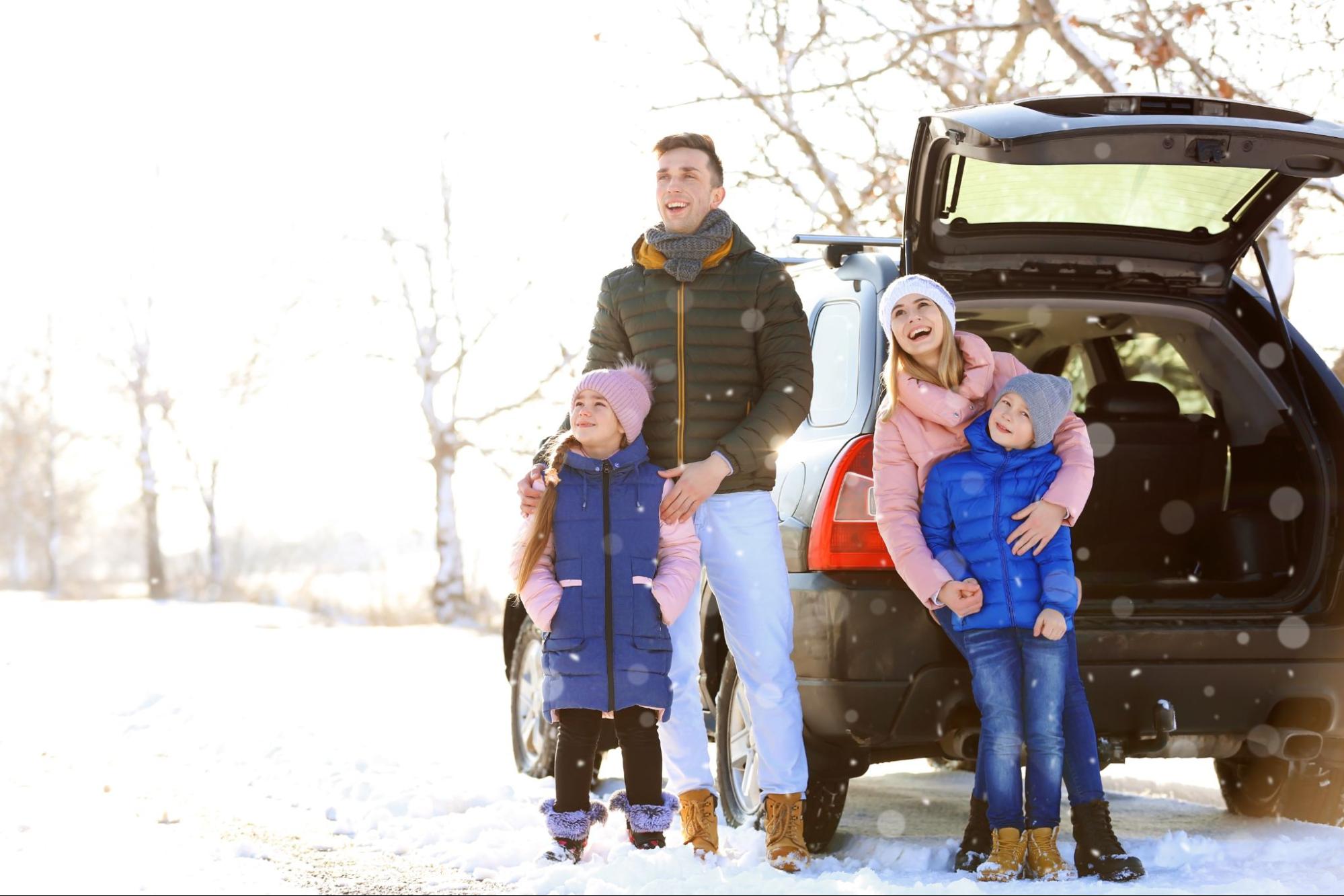 A family standing in front of their car in the snow